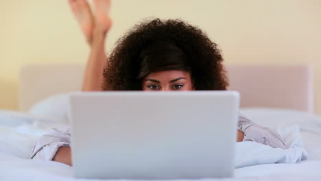 una hermosa morena acostada en la cama usando una computadora portátil