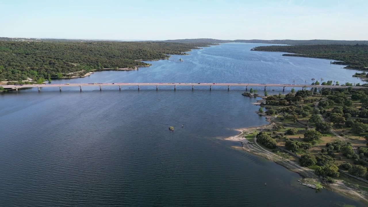 Un lungo ponte si estende su un ampio lago circondato da fitte foreste. La scena cattura le acque calme e la vegetazione lussureggiante, ideale per documentari ambientali.