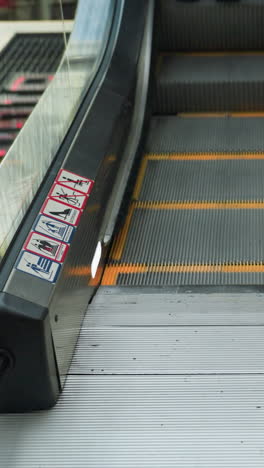 vista en primer plano de dos personas con trajes negros subiendo una escalera mecánica en un centro comercial concurrido. el enfoque está en su movimiento y los detalles de los escalones mecánicos