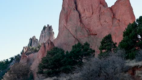drone view of massive red sandstone formations with pine trees in foreground and soft evening light at garden of the gods in colorado springs