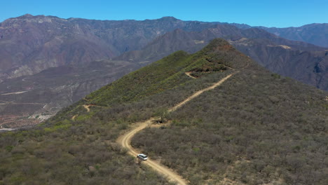 white car driving uphill on dirt road, forward aerial