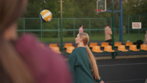 close-up back view of instructor directing volleyball player how to serve, with other people walking outside the court in background, coaching in action on outdoor sports court