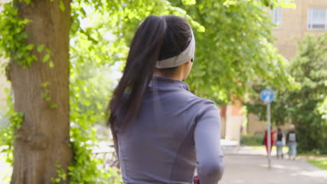 Close-Up-Rear-View-Of-Young-Woman-Exercising-Running-Through-City-Park-Wearing-Wireless-Earbuds-1