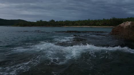 waves crashing and splashing on the rocky shoreline of the fiji islands during early evening - wide shot