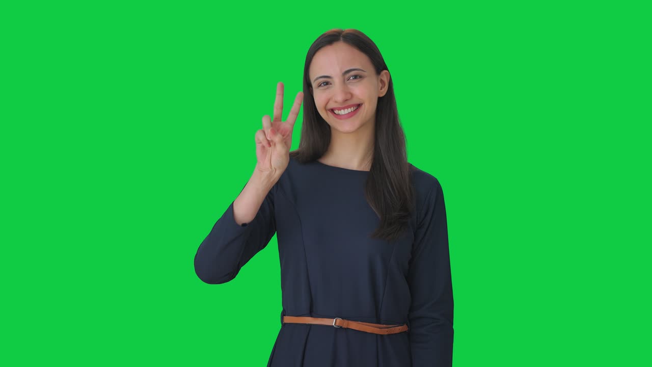 Ragazza indiana felice che mostra il segno della vittoria su schermo verde