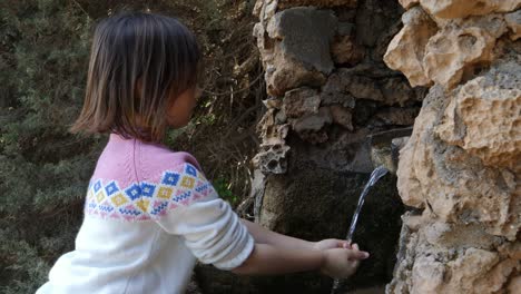 vista media de una linda niña lavándose las manos en un manantial natural
