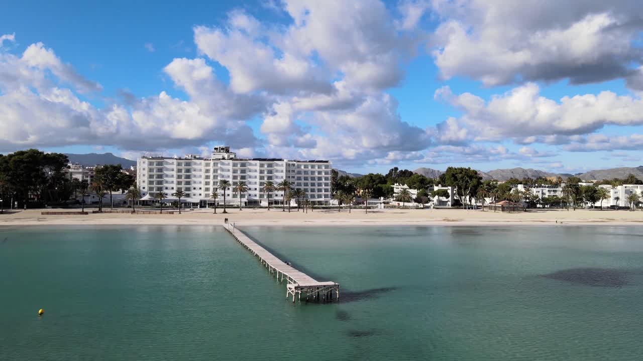 volando hacia abajo hacia el mar azul con nubes y montañas en el fondo detrás de un muelle de madera