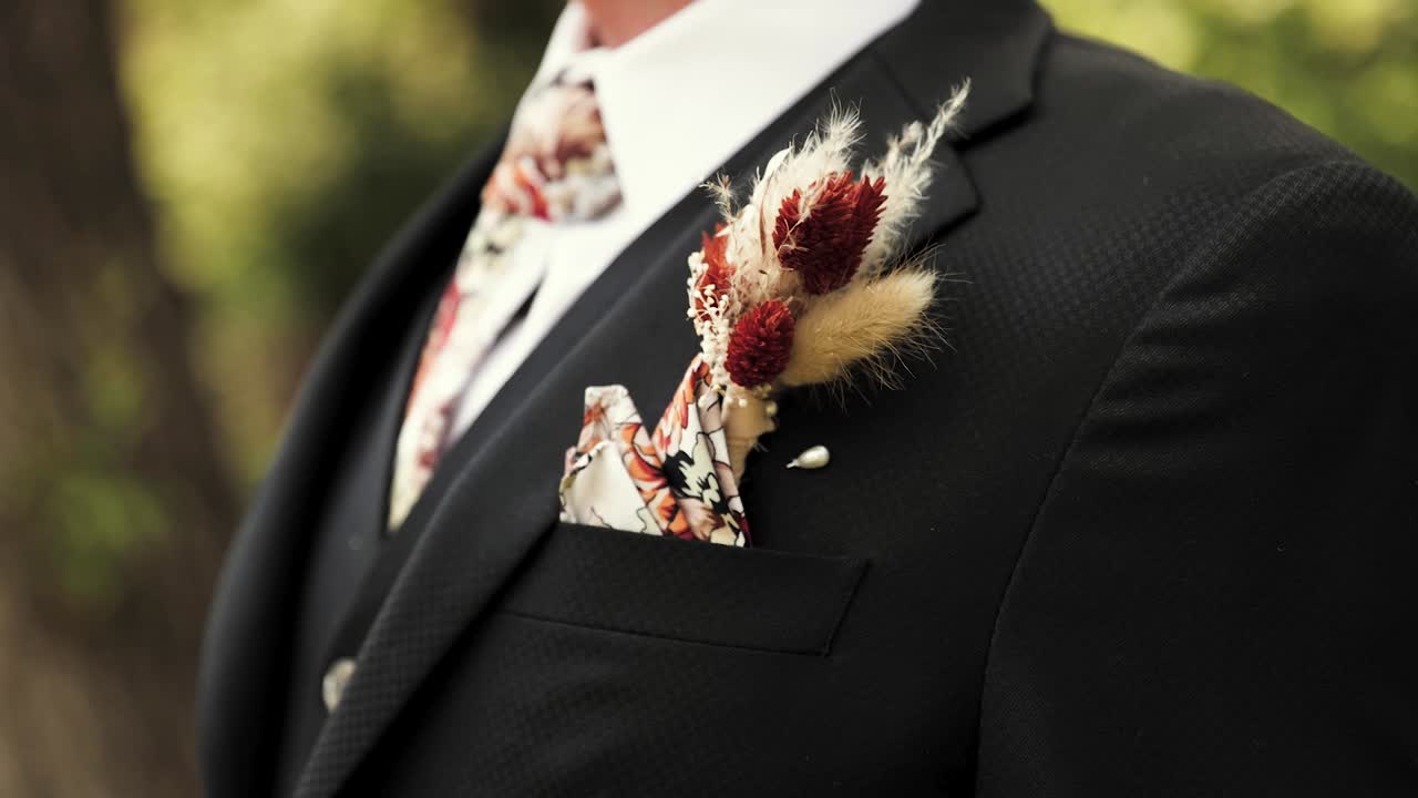 joven o novio parado al aire libre con un traje negro formal con boutonniere único y corbata estampada y bolsillo cuadrado 1080p 60fps