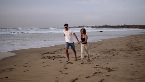 Perfect-scene.-Couple-enjoy-summer-vacation-on-the-large-beach,-enjoy-life-and-running-in-scenery-slow-motion-video-on-background-ocean-landscape.-Young-couple-running-into-tropical-ocean,-happy-smile