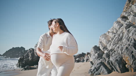 laughing pregnant spouses walking sunny rocky beach feeling happiness close up.