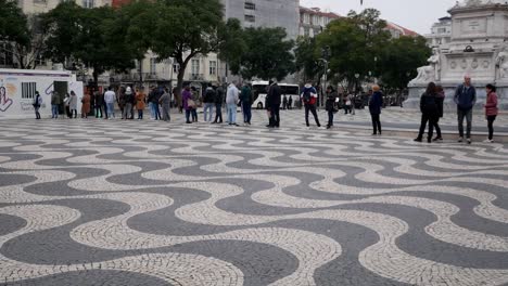covid 19 mobile testing unit at central square, praca dom pedro iv, in lisbon, portugal. people queuing next to monument to get a rapid coronavirus test. typical stoned pavement, mosaic, pattern.