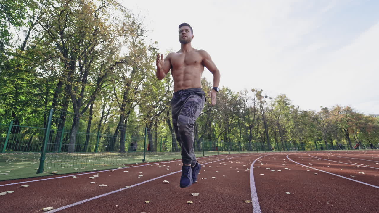 Handsome man training on the field stadium. Young muscular athlete runs on the sports track outdoors. Healthy lifestyle.