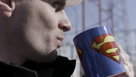 man drinking coffee with superman logo mug outdoors