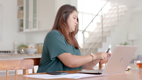 Mujer-Birracial-Ocupada-De-Talla-Grande-Usando-Una-Computadora-Portátil-En-La-Mesa-Del-Comedor,-Trabajando-En-Casa,-Cámara-Lenta