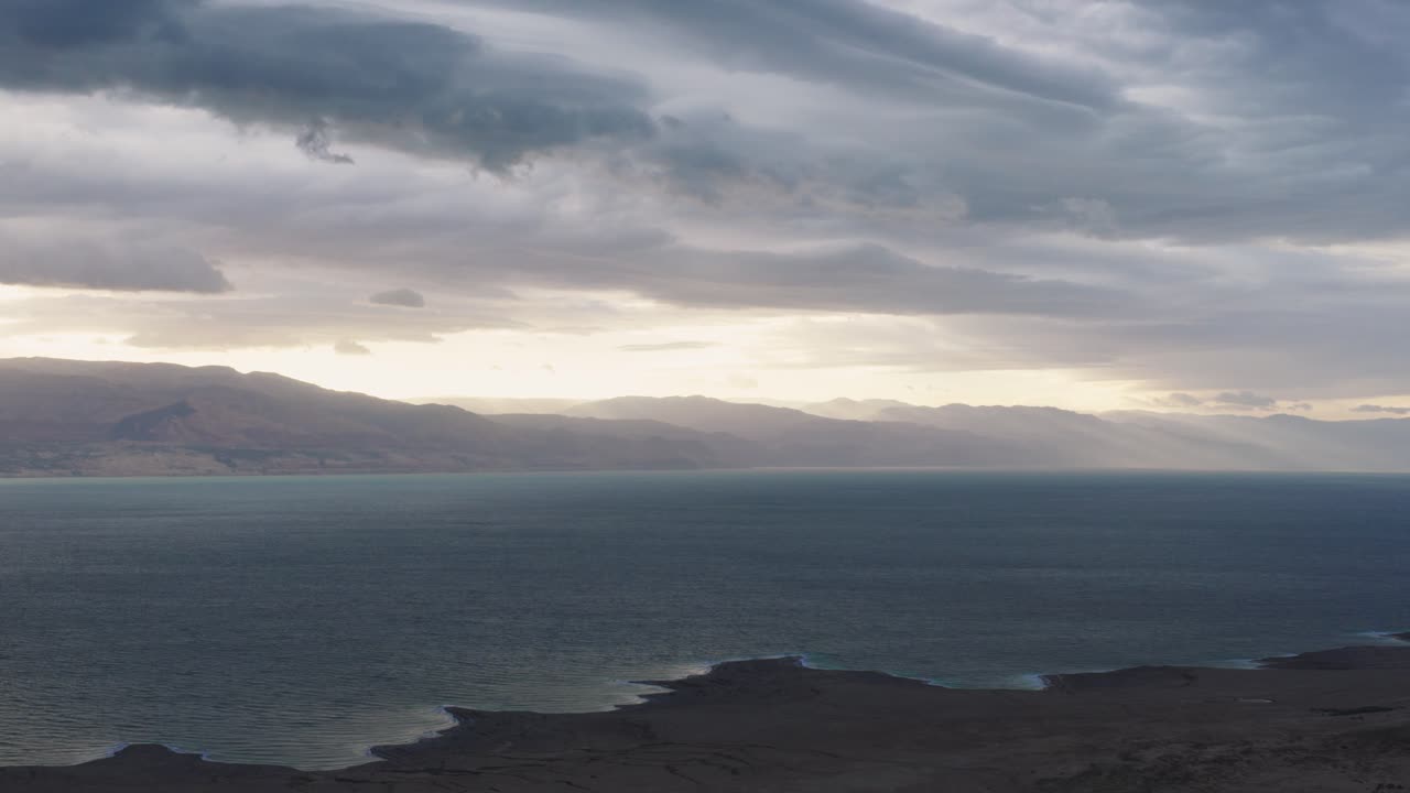 Ampia angolazione aerea della costa del Mar Morto e delle montagne della Giordania illuminate dai raggi del sole che filtrano attraverso le nuvole di una forte tempesta