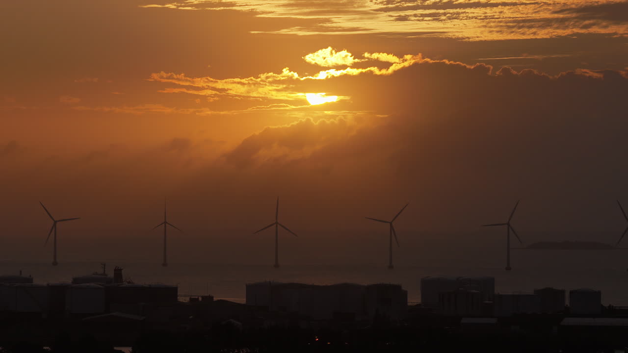 Aerial drone view of the golden sun over the Danish coast, casting light on offshore wind turbines