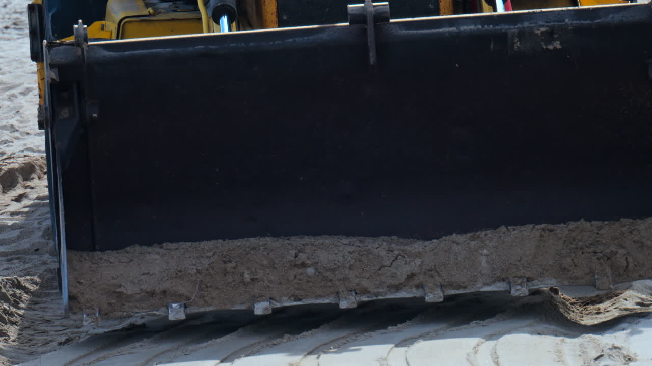 Close up of an yellow wheel loader moving on the sandy beach