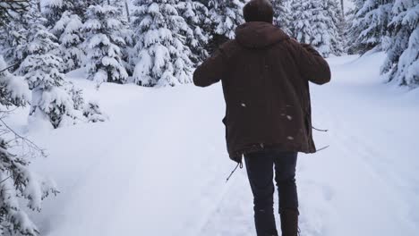 hombre caucásico con ropa informal de invierno caminando por el sendero del bosque invernal y poniéndose una chaqueta marrón de invierno para mantenerse caliente en climas fríos