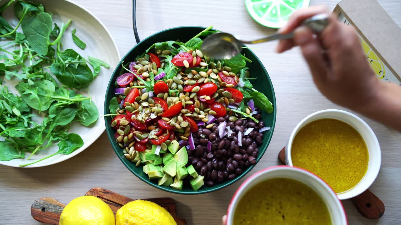Top rotating view aerial shot of salad on platform black beans lemons pumpkin seeds avocado tomatoes leaf spinach dressing