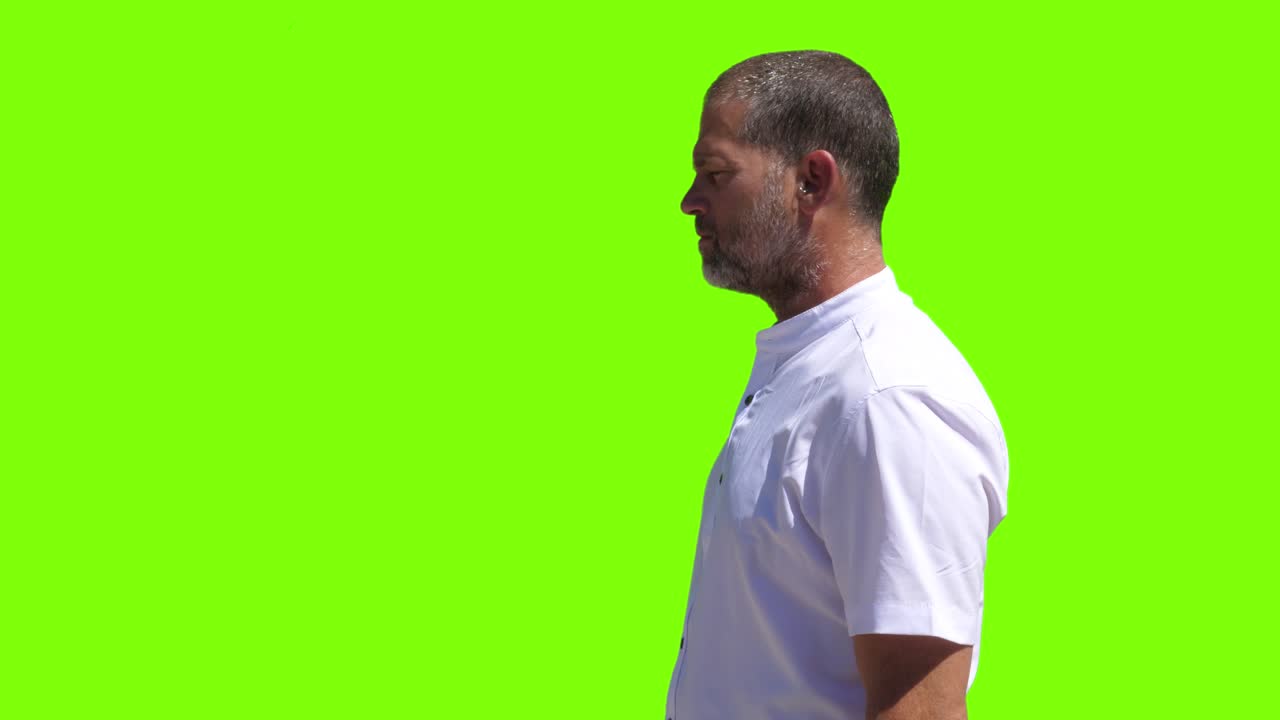 un hombre diligente en movimiento, posicionado contra una pantalla verde, mira hacia los lados mientras manipula hábilmente botones virtuales