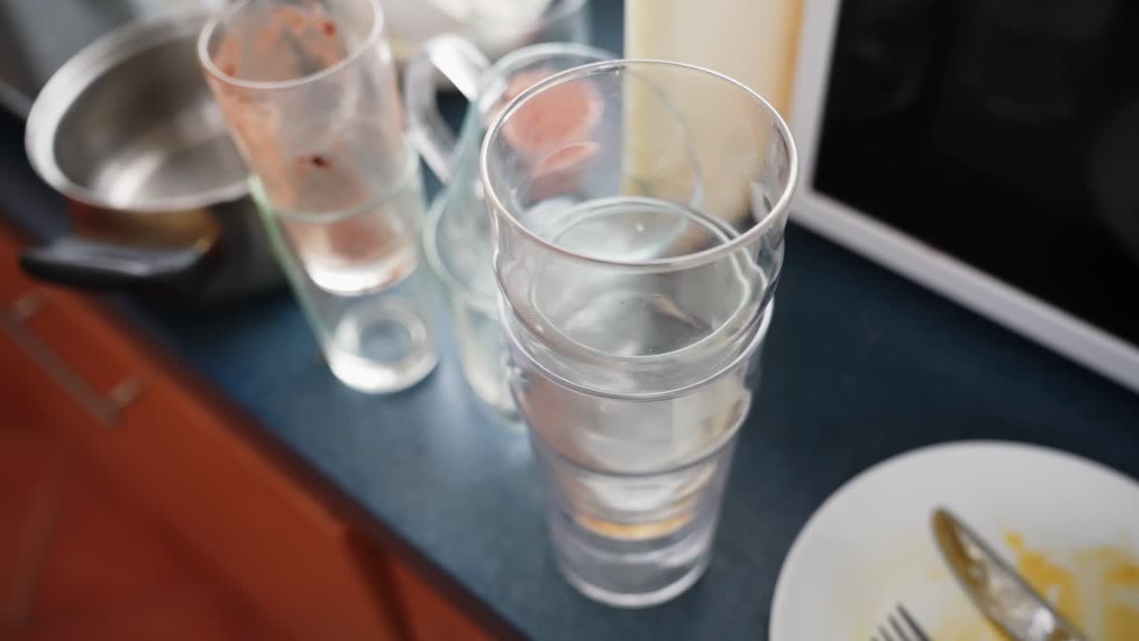 Piano di lavoro di una cucina disordinato con pentole sporche, tazze e bicchieri vuoti accanto a un forno a microonde, resti della colazione in attesa di essere lavati, faccende domestiche quotidiane a casa