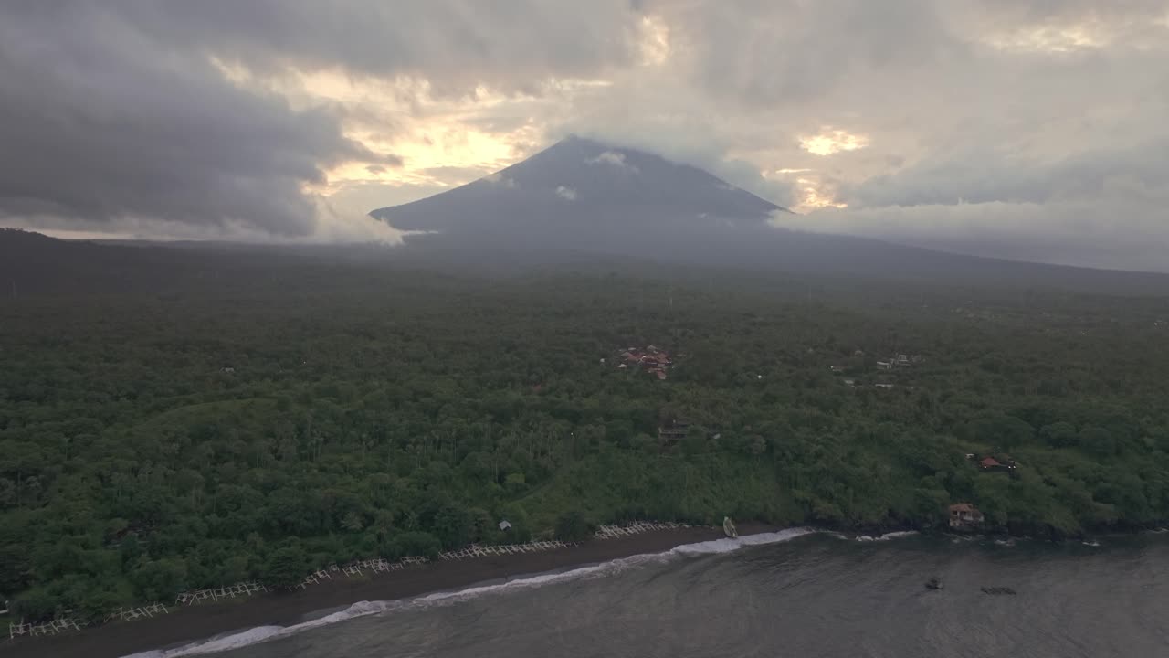 Vista aérea do pôr do sol em Bali sobre a praia de Amed, com barcos de pesca, moradores locais e o Monte Agung imponente.