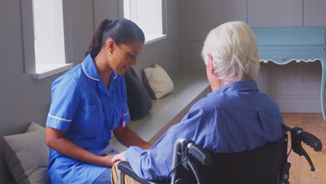 senior man at home in wheelchair talking to female care worker in uniform who makes notes