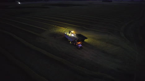 grain unloaded onto semi truck with trailer at night in farm land, aerial