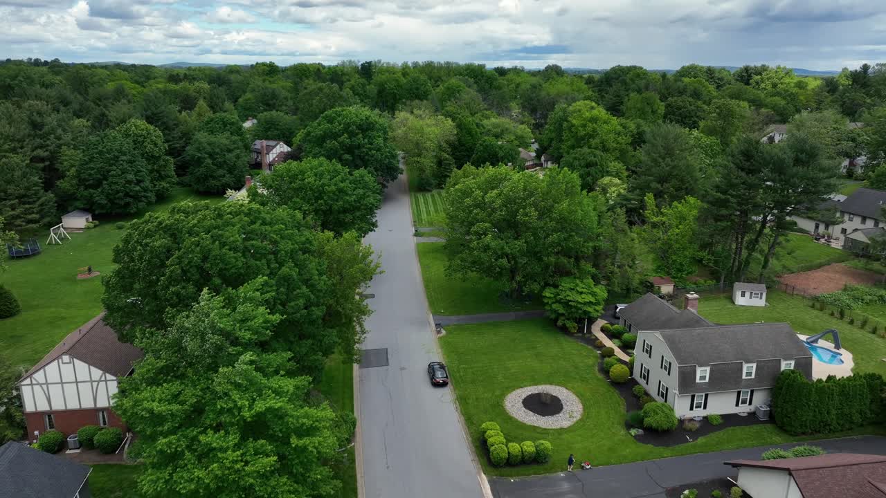 Upper class residential area with swimming pool in garden. Driving car on street of charming american neighborhood.Cloudy spring day with green trees and tutored lawns in yards. Suburb district.Aerial