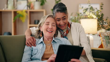 mujeres mayores riendo juntas en un sofá usando una tableta