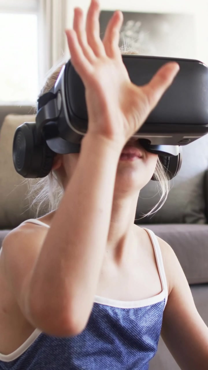 Video verticale: Ragazza con top blu che si allunga con visore VR nero sul divano, coprendosi gli occhi e interagendo con la scena VR.