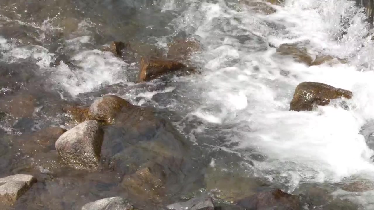 Ripresa statica dall'alto di acqua fresca di fiume che schizza sulle rocce alla luce naturale del giorno.