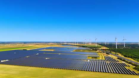 lots of solar panels installed in the countryside. wind farms work at backdrop. aerial view