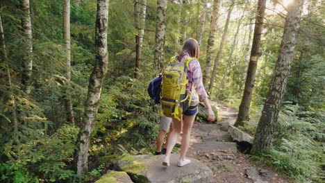 Young-Tourists-With-Backpacks-Walk-Along-A-Trail-In-The-Forest