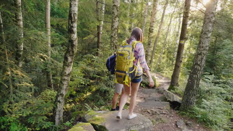 young tourists with backpacks walk along a trail in the forest