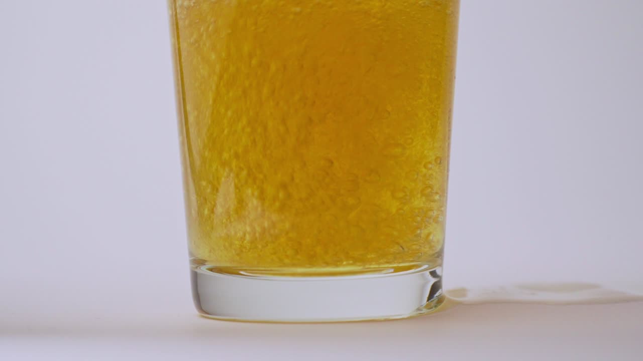 Ripresa al rallentatore di birra versata in un bicchiere, che mostra bollicine, schiuma e movimento dettagliato del liquido