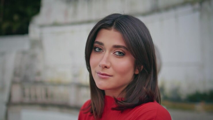 Primo piano di un volto femminile che si gira verso la telecamera sorridendo. Donna sicura di sé in abito rosso all'aperto.