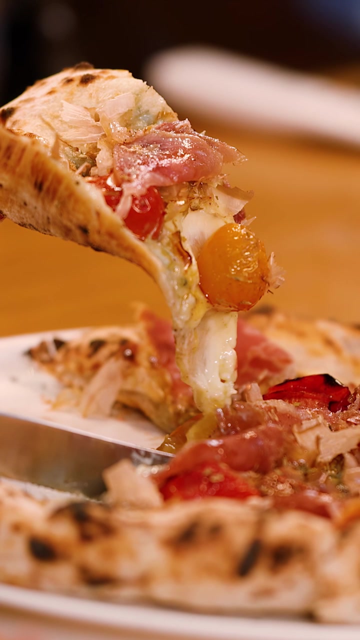 Primo piano di una mano che taglia una pizza gourmet con un coltello e solleva una fetta filante.