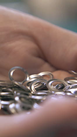 cu: skilled tailor pours on hand various silver eyelet parts from blurry transparent jar in workshop close view