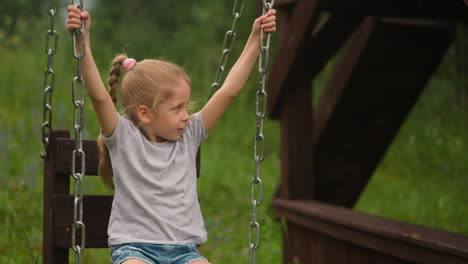 Happy-little-girl-with-braid-plays-wooden-swings-on-ground