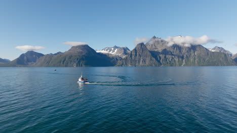 Fishing-boat-sailing-on-blue-sea-water-of-Lyngen-fjord-with-rocky-mountains-of-Scandinavian-Alps-in-background-on-sunny-day,-Norway