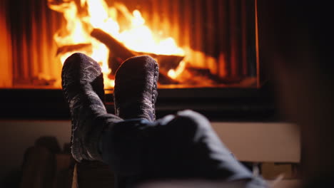 los pies en calcetines contra el fondo de la chimenea se mantienen calientes junto al fuego vivo