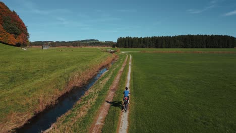 Eine-Junge-Frau,-Die-Mit-Einem-Tourenrad-Auf-Einer-Grünen-Wiese-In-Der-Herbstlichen-Natur-In-Bayern-Radelt