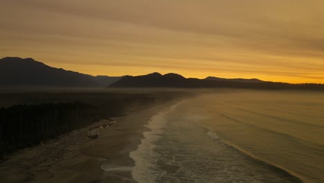 stunning golden sunset above bruce bay with waves hitting shore, aerial