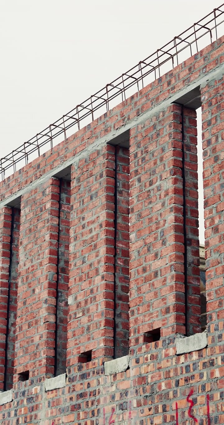 Obra en construcción con pared de ladrillo sin terminar y varillas de refuerzo expuestas