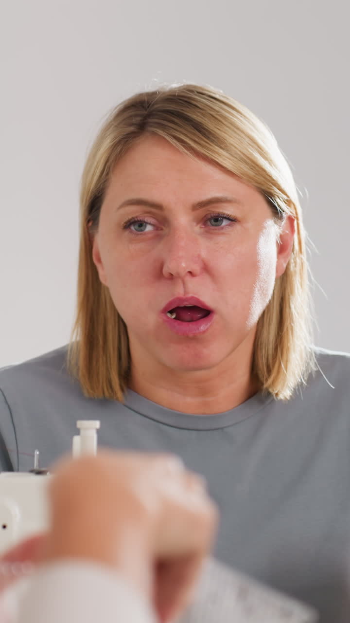 Worker enjoying break, Lady having snack with colleague at workstation, Female worker with light hair taking brief break while discussing tasks at her sewing station during rest period