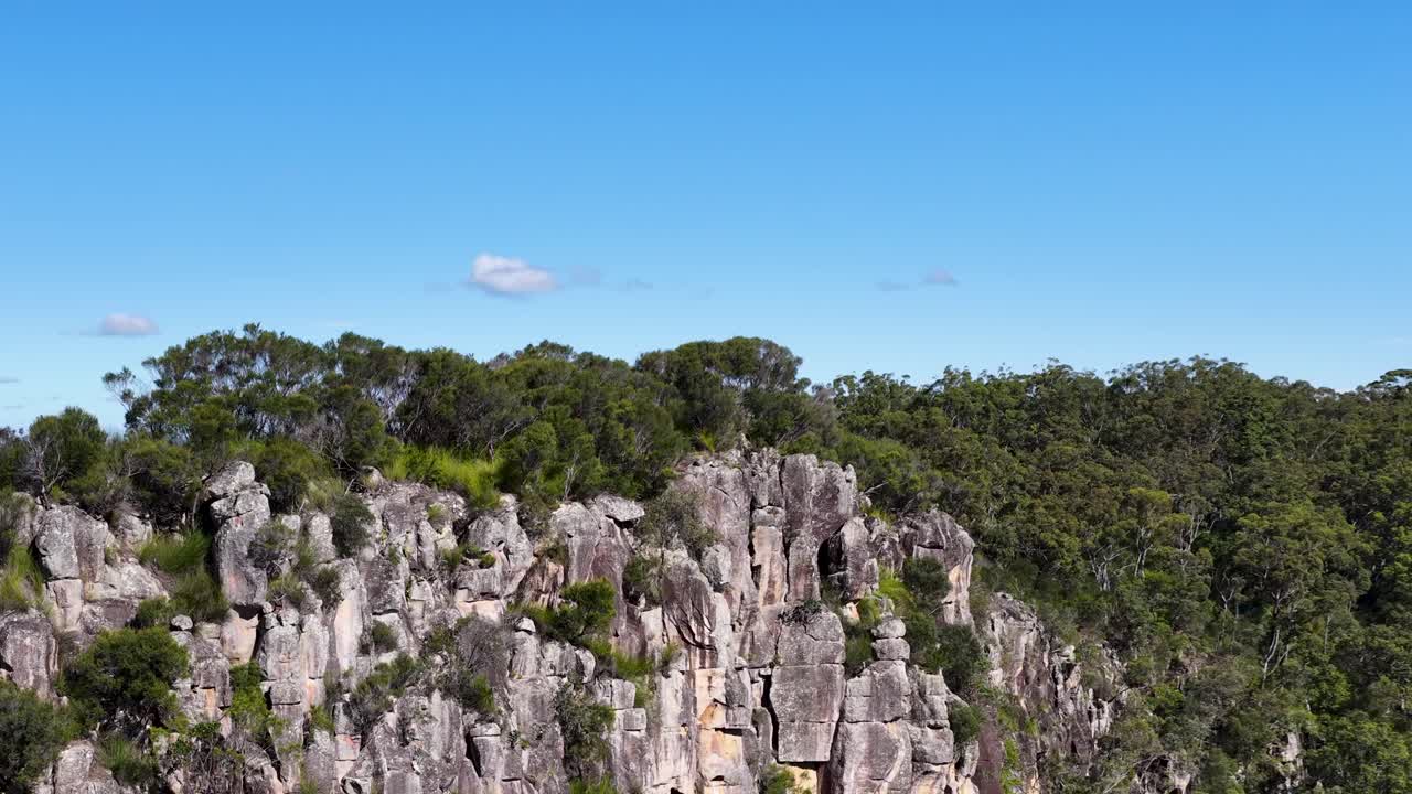 Drone captures panoramic view of Nimbin Rocks, showcasing lush greenery and unique rock formations under bright blue skies