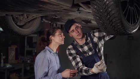 Handsome-young-auto-technician-explaining-to-a-young-female-client-what-repair-process-was-made.