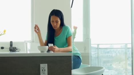 Woman-using-mobile-phone-while-having-breakfast-in-kitchen-4k