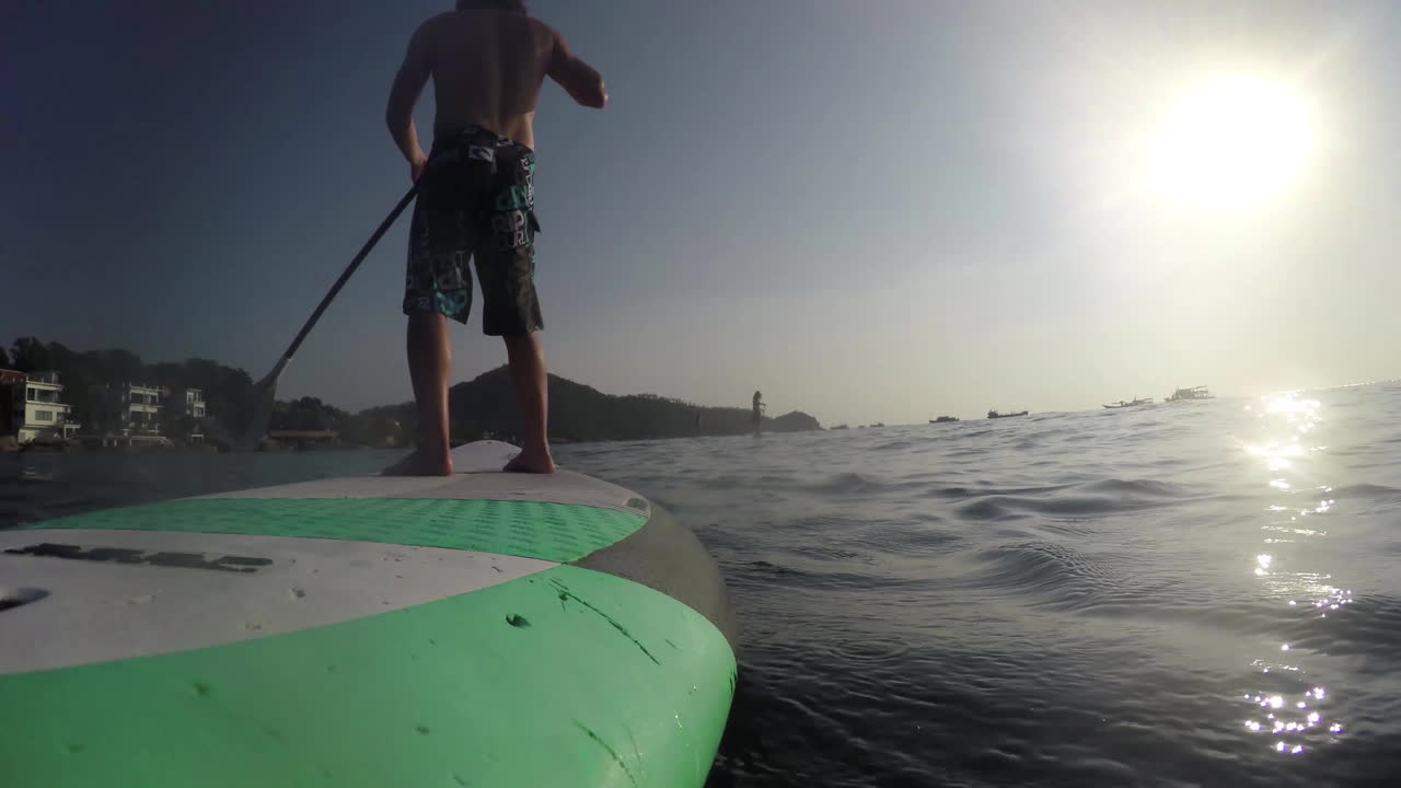Sup board riding. The camera is mounted on the back of the board. In the foreground a man rowing an oar